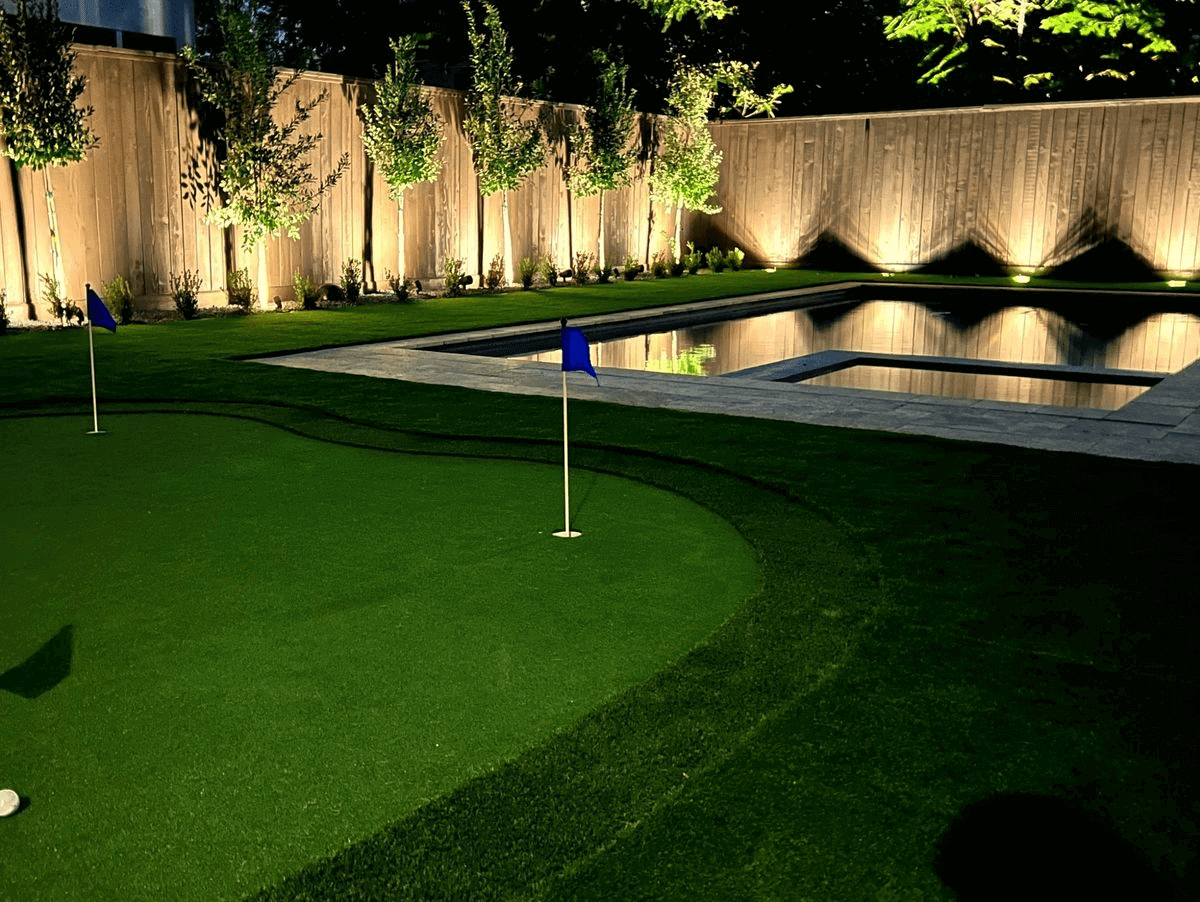 Backyard with putting green and illuminated pool.