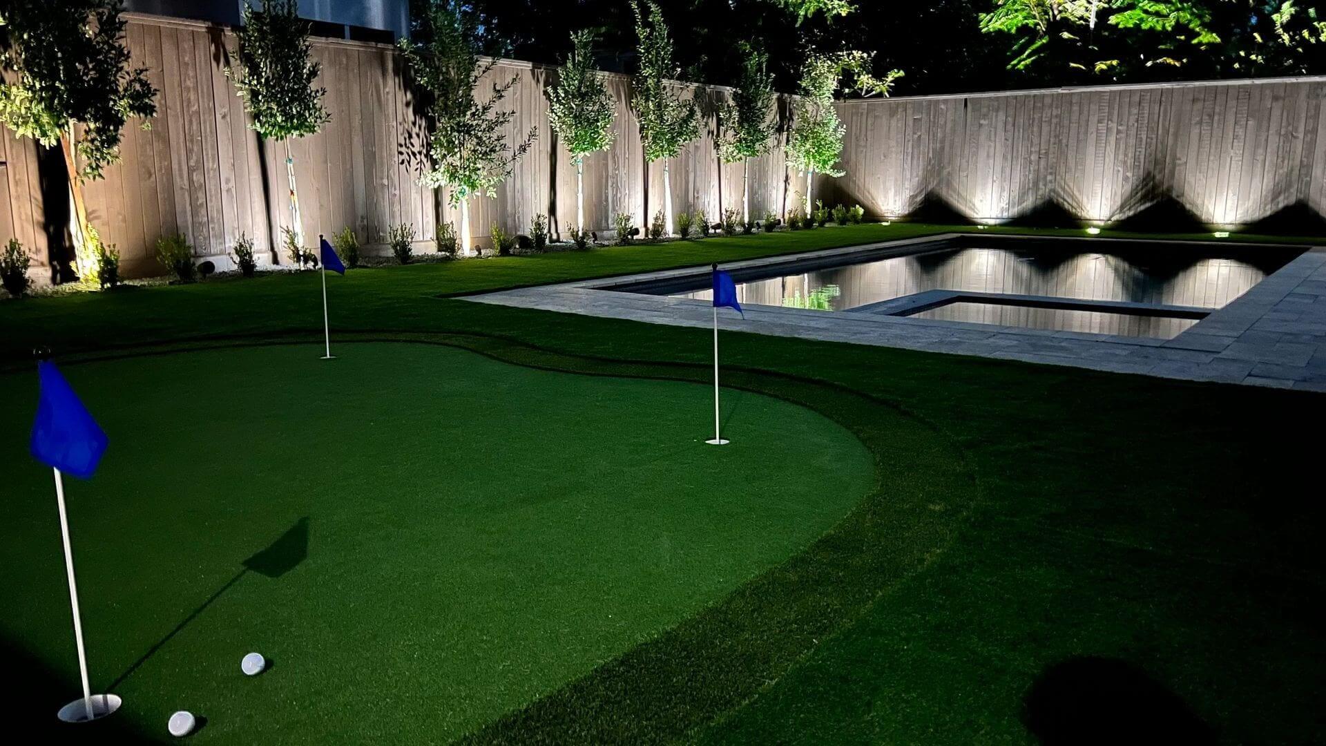 Backyard golf green and pool at night.