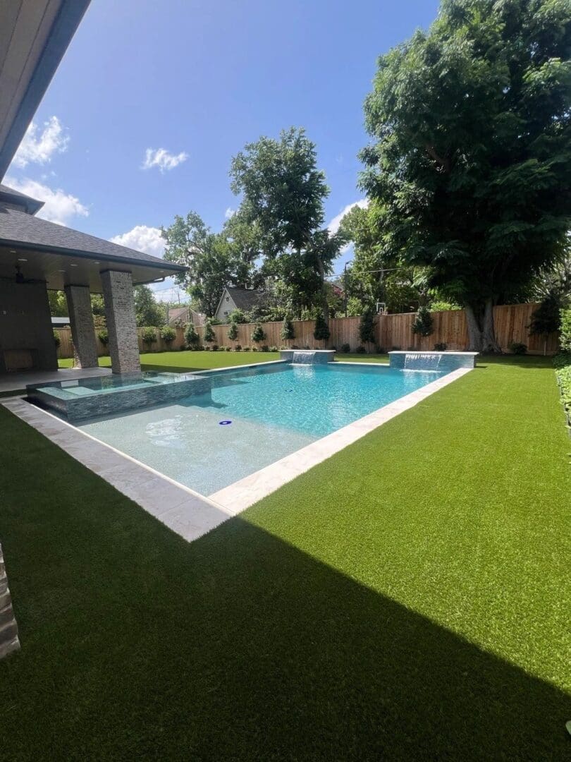 Backyard pool with artificial grass and trees.