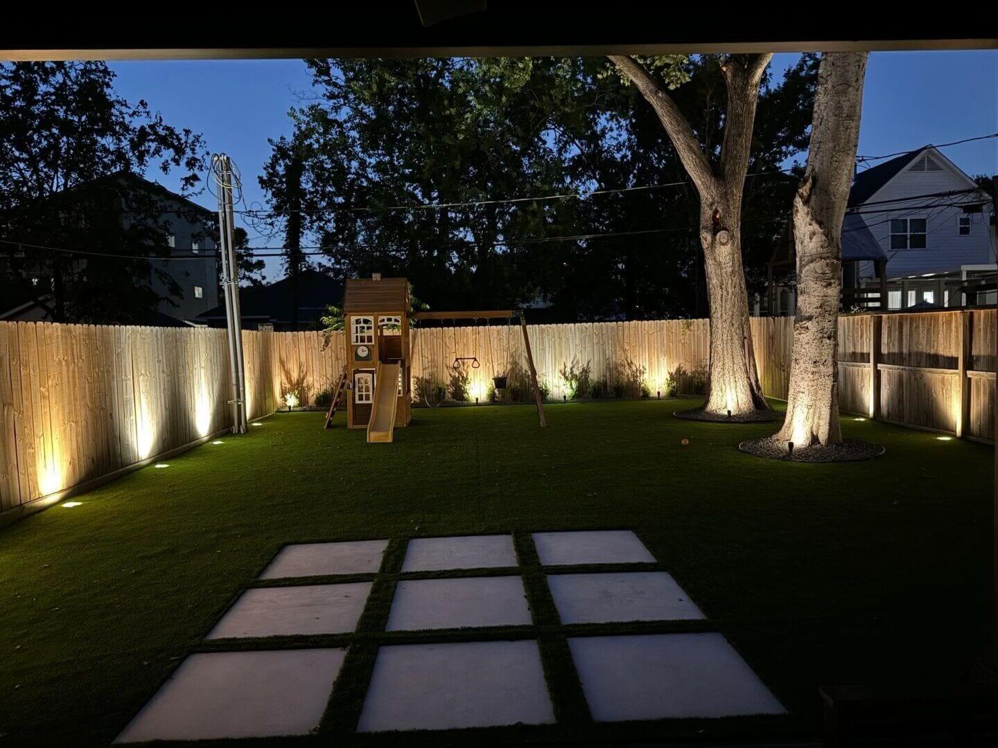 Backyard playground with evening lights and trees.
