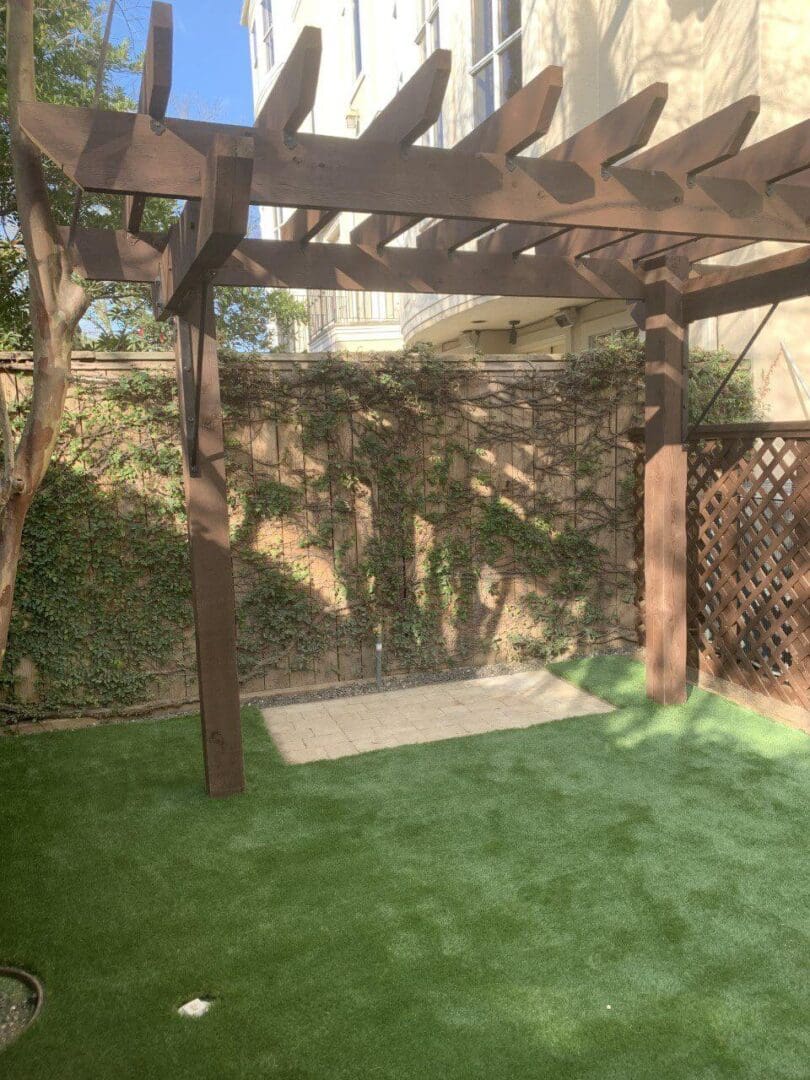 Sunlit backyard with artificial grass and wooden pergola casting shadows.