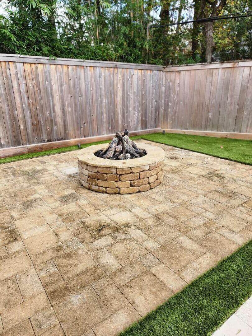 Backyard with stone fire pit and patio surrounded by lawn and wooden fence.