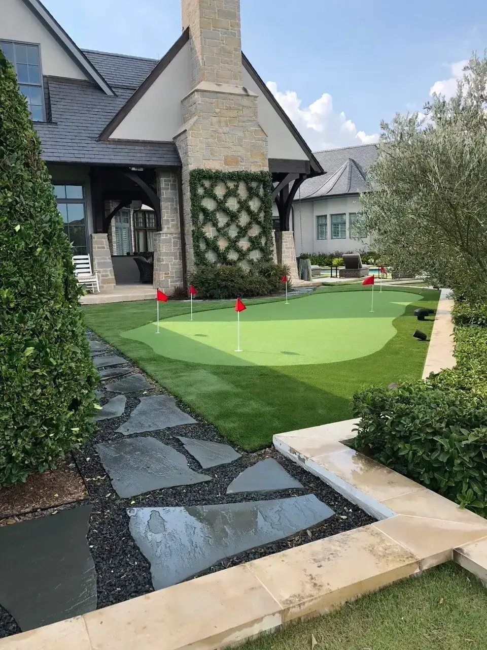 A backyard with a small artificial putting green and stone pathway.