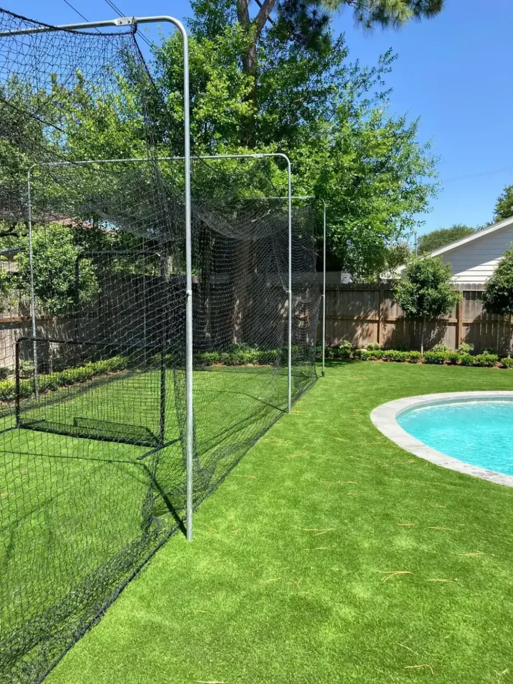 A backyard with a pool and a large net enclosure on artificial grass.