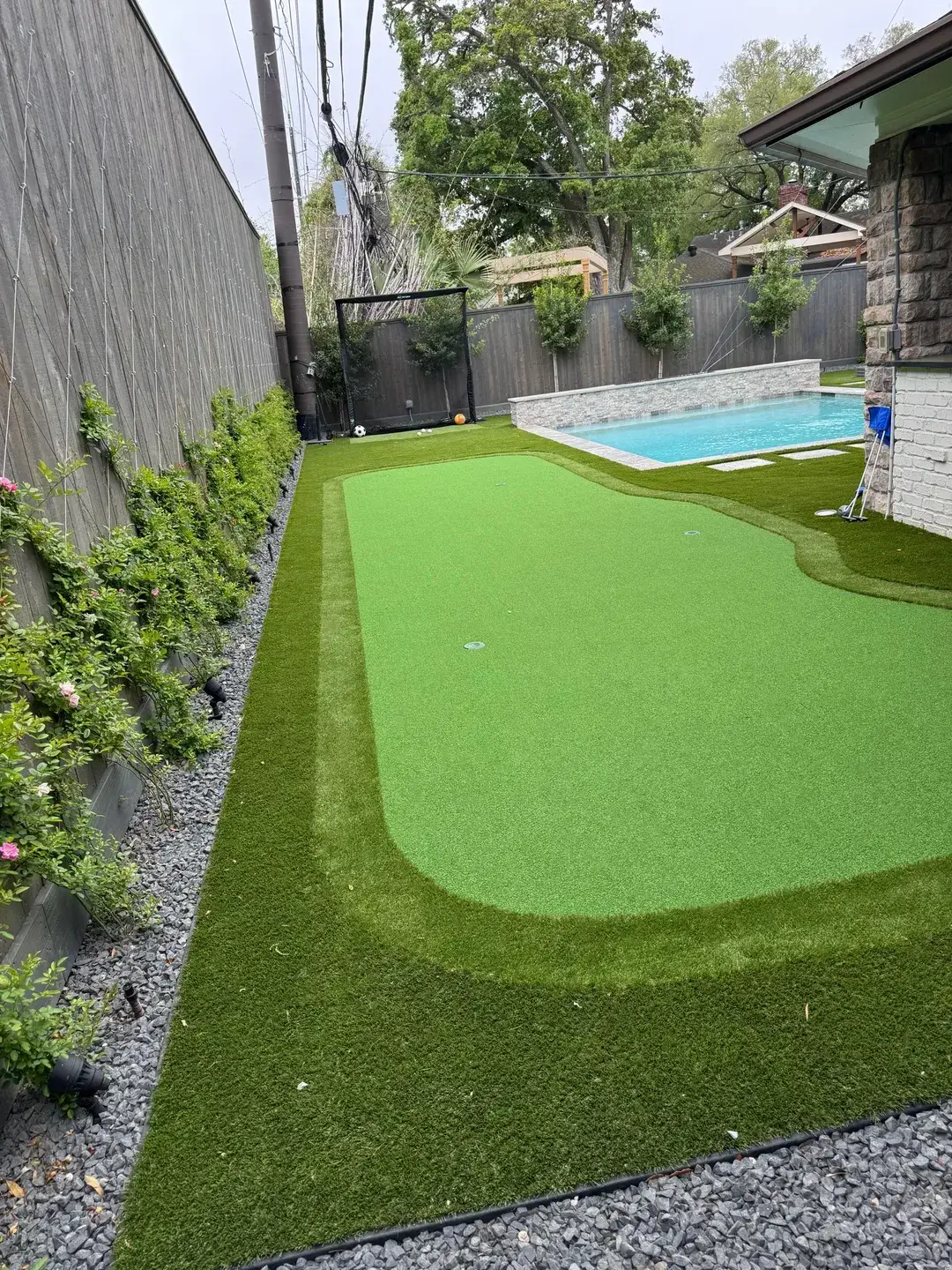 Artificial turf with a putting green next to a pool in a backyard.